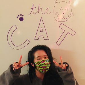Masked volunteer standing if front of theCAT logo
