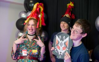 Three students pose with piñata fragments showing a logo of a robotic cat.